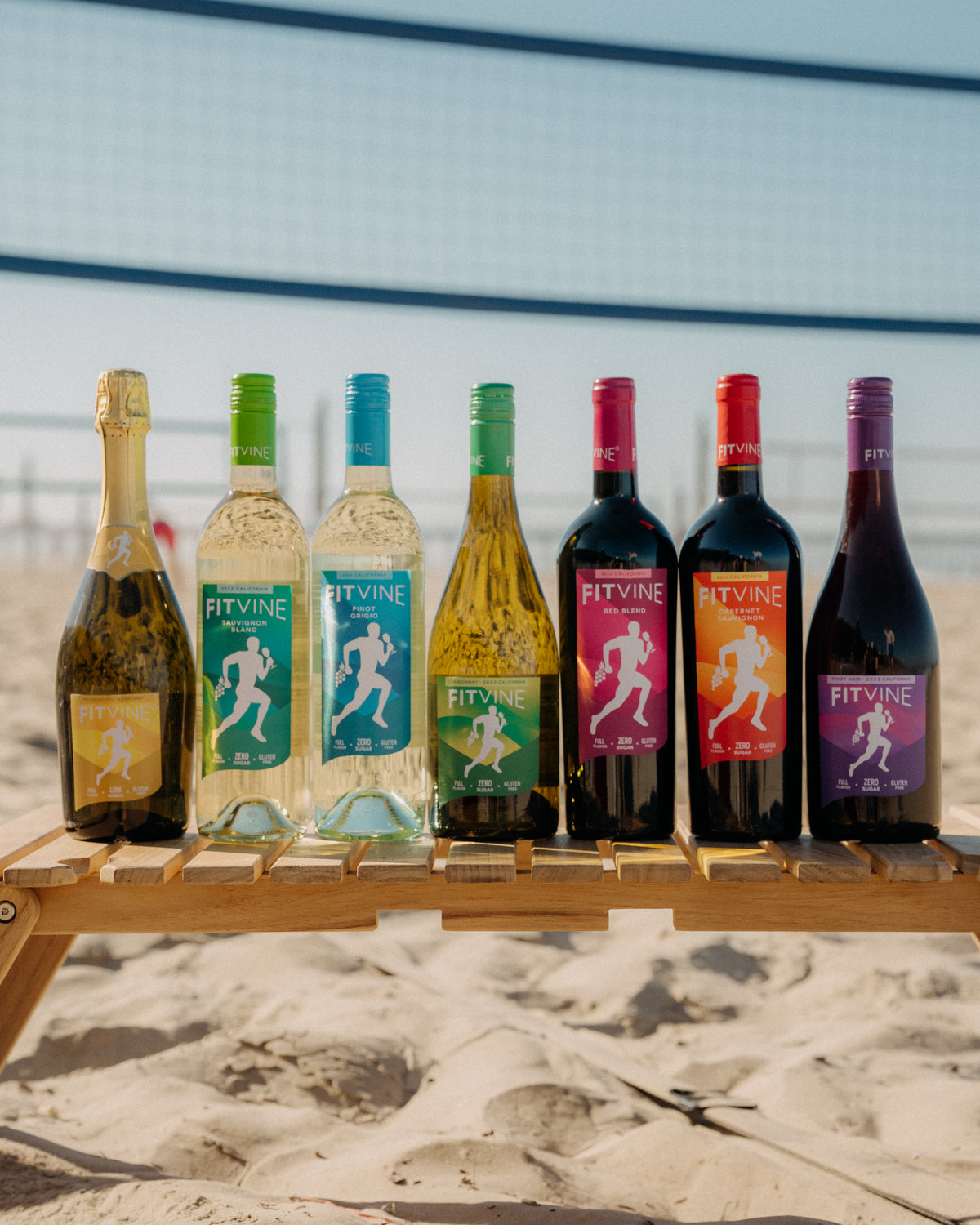 Set of FitVine wine bottles on a wooden stand with a beach background